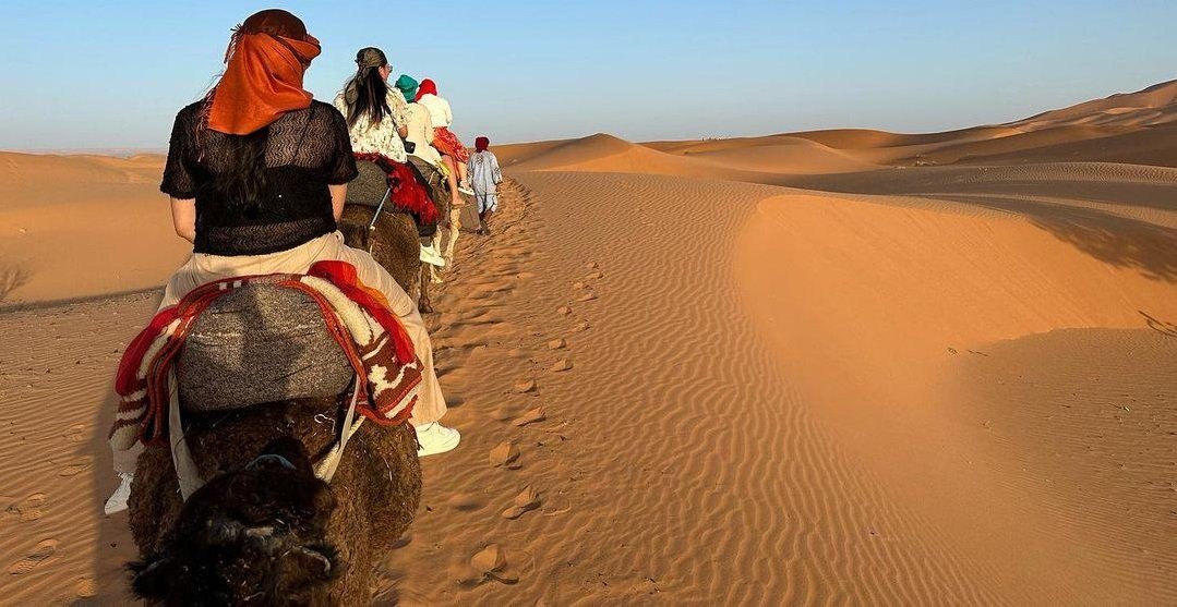 Tourist riding camel in Sahara Desert Morocco wearing long sleeves and scarf