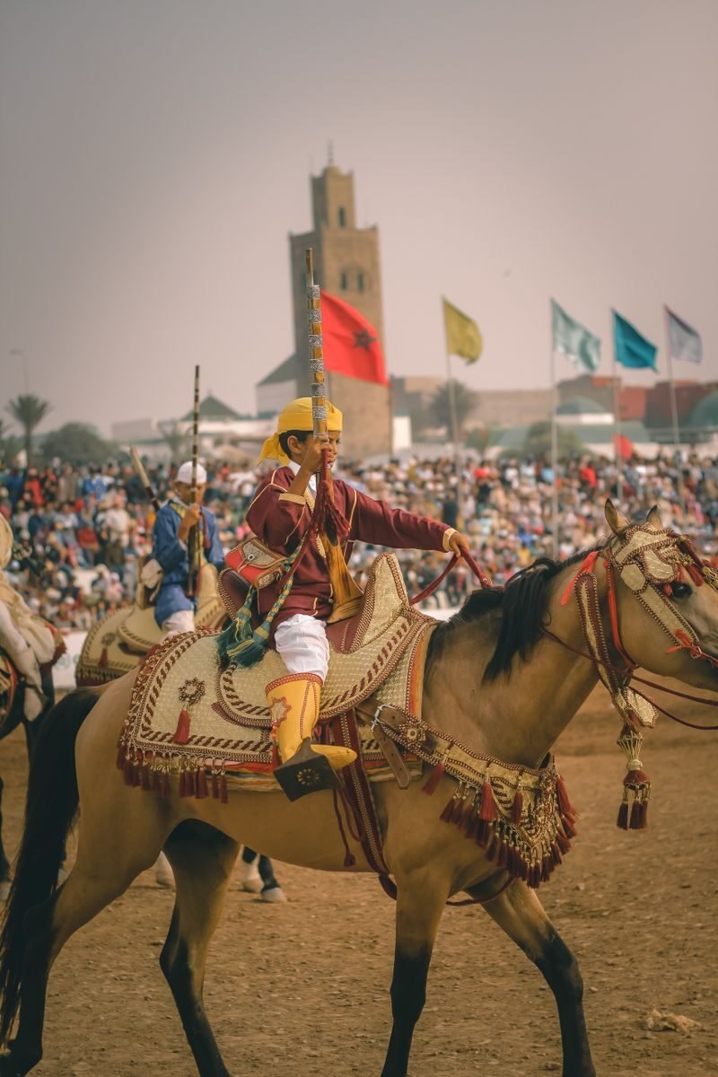 Photo by Photographic SABER Crowds gather at a Moroccan festival featuring traditional horse riding performances with vibrant cultural displays.